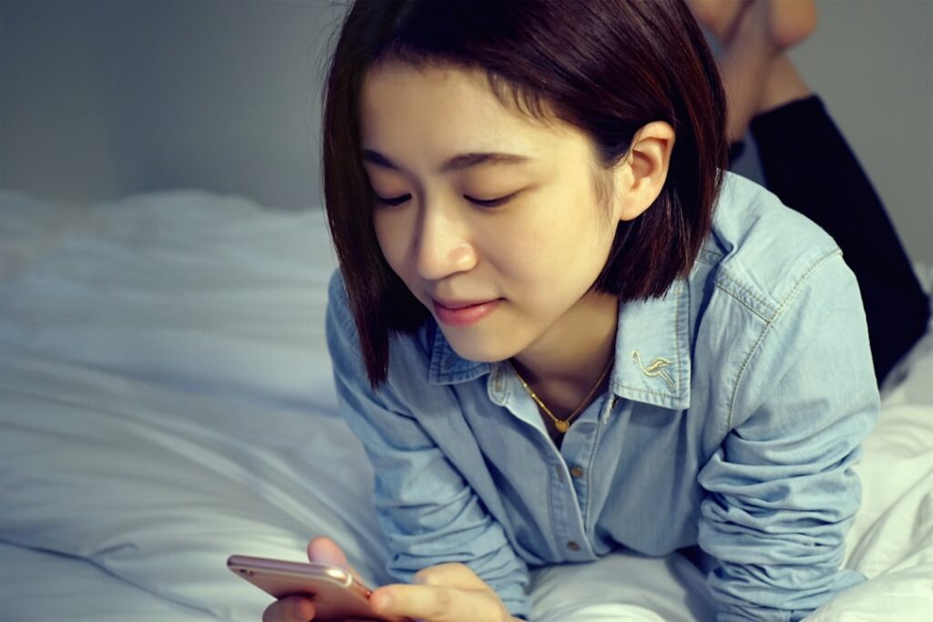 young japanese woman thinking on bed smartphone