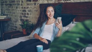 young woman smartphone evening bedroom