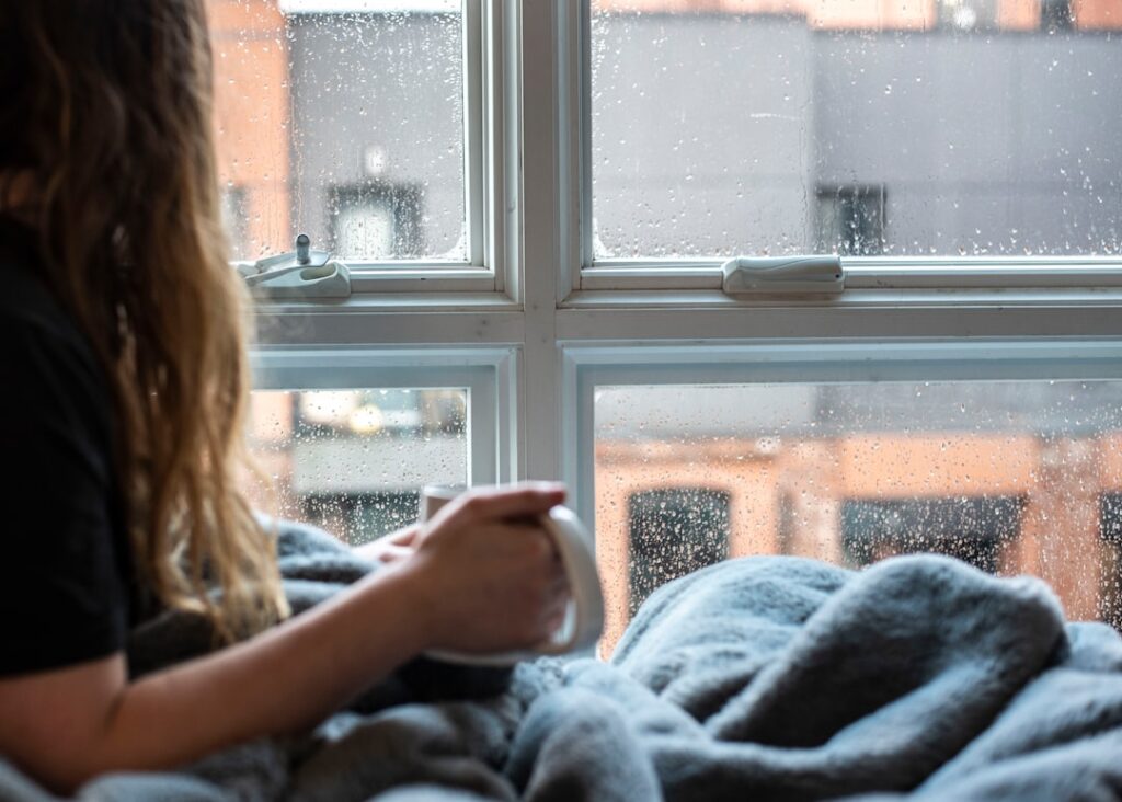 woman looking out rainy window alone